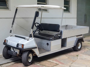 A parked two-seat golf cart with a truck bed for transporting materials.