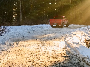 Pick-up truck driving on slushy, snow covered road surrounded by trees.