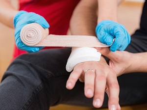 One person wearing gloves wrapping a cut on another person's hand, providing first aid.