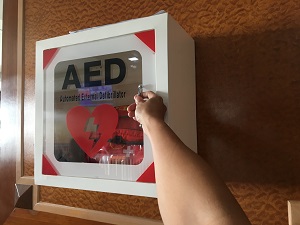 Person reaching for an AED in a wall cabinet.