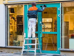 Worker standing on step stool fixing a door on a business.