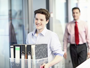 Young worker carrying a box filled with binders through an office building.