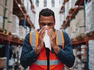 Sick Warehouse Worker Sneezing into a Tissue