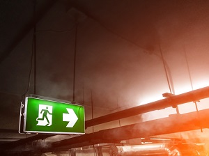 Illuminated Exit Sign Inside Building with Fire and Smoke Visible