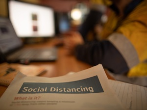 Worker at Computer that has Social Distancing Information on Desk