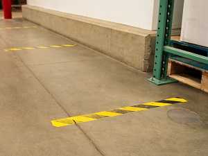 Yellow and Black Tape on Floor of Warehouse Spaced 6 Feet Apart