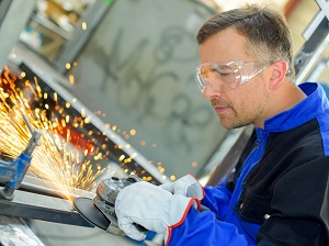 Worker Wearing Gloves and Safety Glasses Using Portable Grinder on Metal in Shop, Sparks Flying