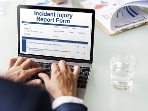 Worker Filling Out Incident Injury Report Form on Laptop