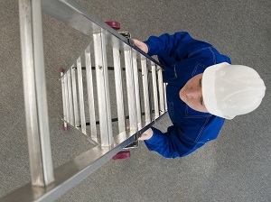 A vew from above of a worker wearing a hard hat climbing a step ladder.