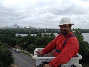 Worker inside an elevated bucket truck. He is wearing a harness and the attachment point has a lanyard connected.