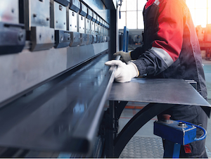 Press brake operator positioning a sheet of metal on a press brake table while wearing protective gloves.