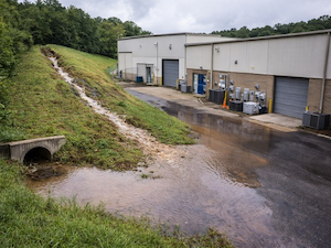 Commercial facility with water pooling near a drainage ditch and building exterior, showing flood risk from runoff.