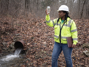 Environmental worker collecting a stormwater sample near a drainage pipe.