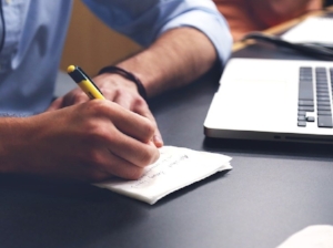 Office Worker Taking Notes on Paper, Laptop Nearby