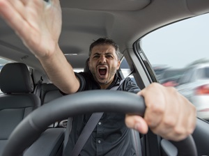 A man driving in traffic is visibly angry while yelling.