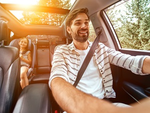A man is driving safely while his young child is in a car seat in the back.