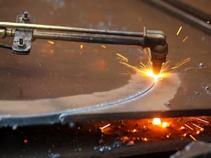 Oxy-fuel cutting torch slicing through a thick sheet of metal with visible sparks and molten metal.