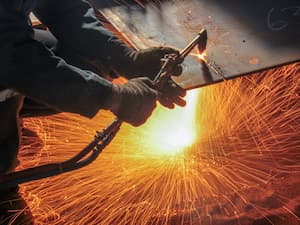 Worker using a cutting torch with intense orange sparks flying in all directions during the cutting process.