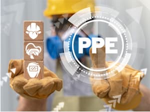 Worker wearing protective gloves holding blocks with PPE icons, including hard hat, gloves, and respirator, with digital 'PPE' overlay.