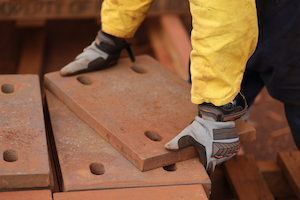 Worker wearing gloves lifting heavy steel plates demonstrating proper hand protection.