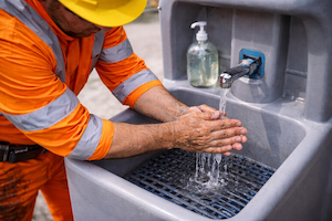 Construction worker washing hands at a jobsite sink to maintain hygiene after asphalt work.