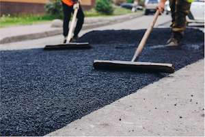 Workers using rakes to spread and level freshly laid asphalt during paving operations.
