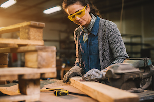 Worker wearing gloves and safety glasses sanding wood in a workshop.