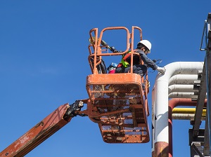 Worker on an aerial lift performing pipe maintenance.
