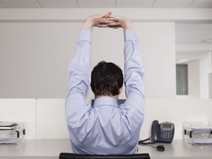 An office worker stretching while sitting at a desk.
