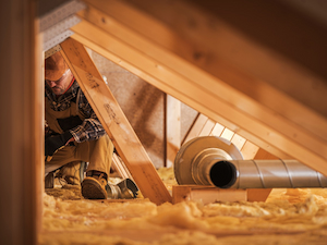Worker in an attic crawl space surrounded by insulation during hot working conditions in a confined area.