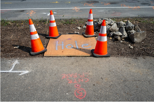 Covered construction hole marked with cones to warn workers of a fall hazard.