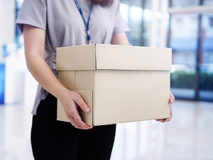 Professional woman holding box, walking through office building.