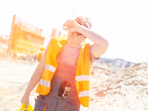 Construction worker shielding face from intense sunlight and heat while working outdoors in high temperatures.