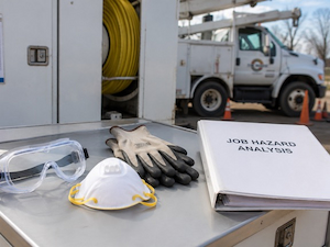 Safety goggles, dust mask, work gloves, and a Job Hazard Analysis binder arranged on a utility truck before starting work.