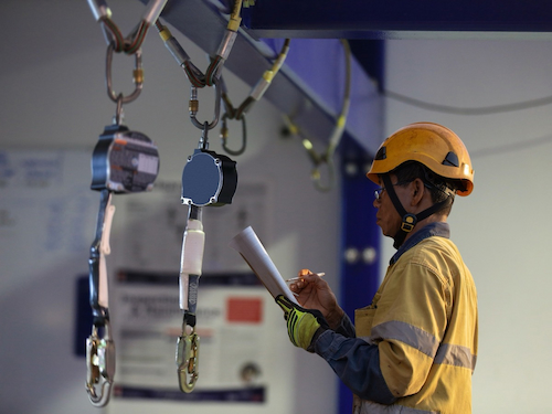 Worker inspecting self-retracting lifelines as part of a fall protection equipment inspection.