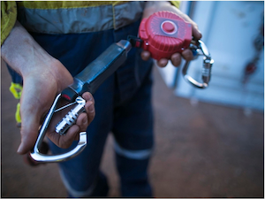 Worker inspecting the connector and locking gate on a self-retracting lifeline before use.