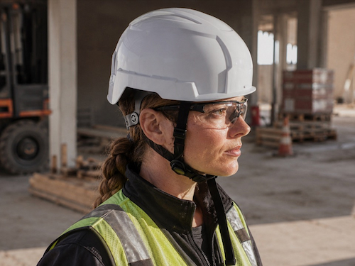 Construction worker wearing a white industrial safety helmet with chin strap, safety glasses, and high-visibility vest.