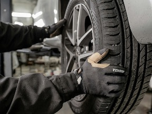 Mechanic wearing protective gloves while inspecting a vehicle tire in an auto repair shop