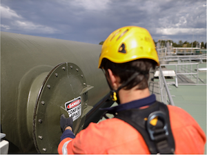Worker wearing fall protection preparing to enter a confined space through a tank access hatch.