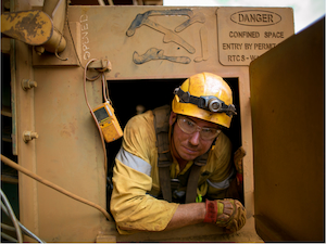 Worker wearing a harness and hard hat exiting a permit-required confined space.