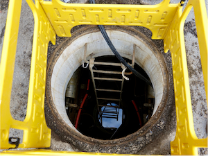 Open manhole with ladder surrounded by a protective safety barrier.