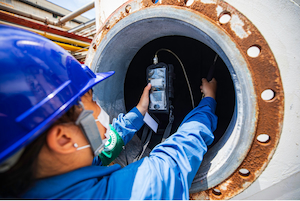 Worker using a remote sampling probe and portable gas monitor to test the atmosphere inside a confined space before entry.