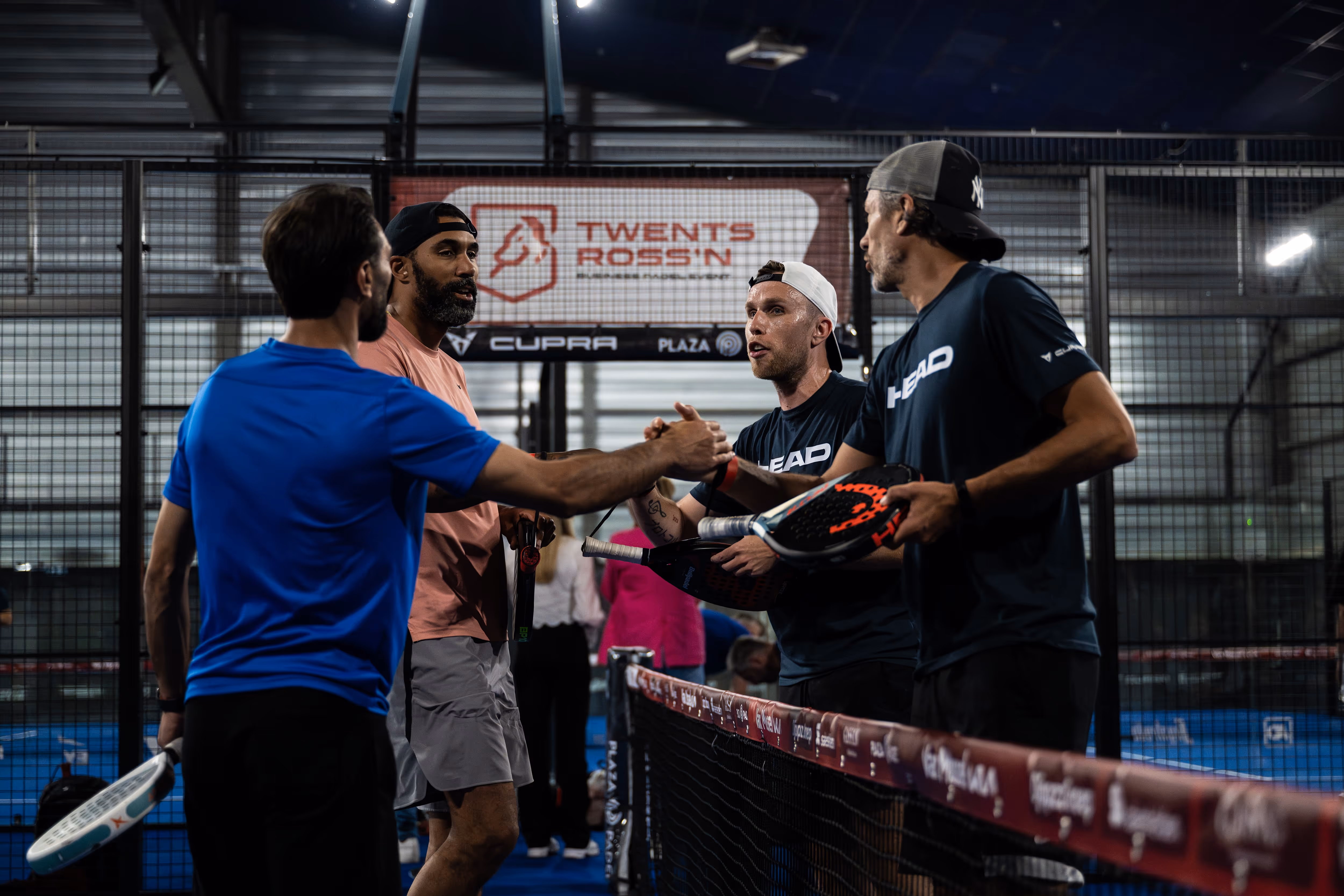Vier mannen geven elkaar een handdruk op een padelveld tijdens een B2B sportevenement