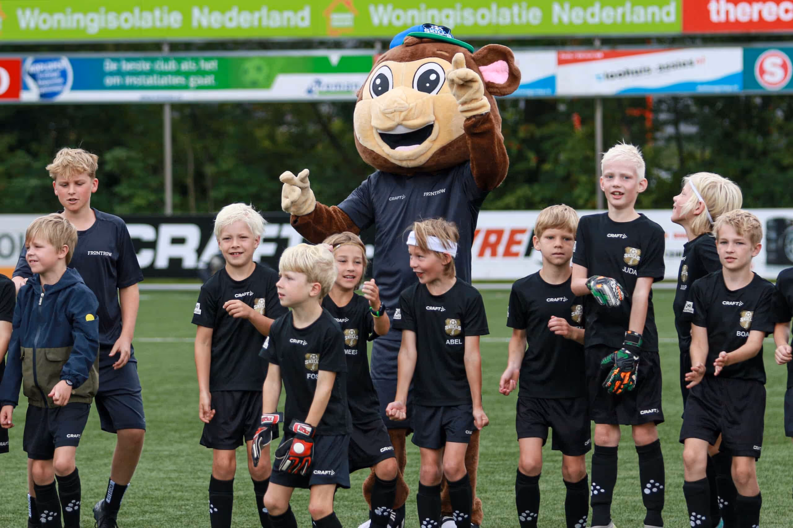Een groep vrolijke kinderen met mascotte Binkie tijdens een B2C sportevenement op het voetbalveld