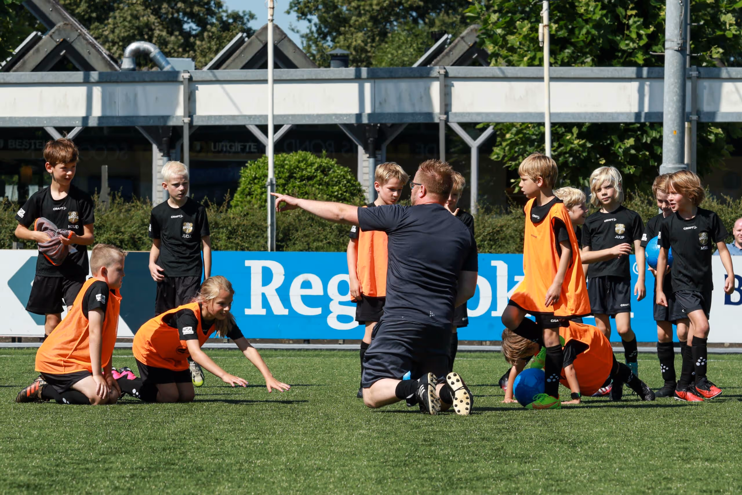 Een sportprofessional op het voetbalveld die instructies geeft aan kinderen tijdens een voetbalclinic