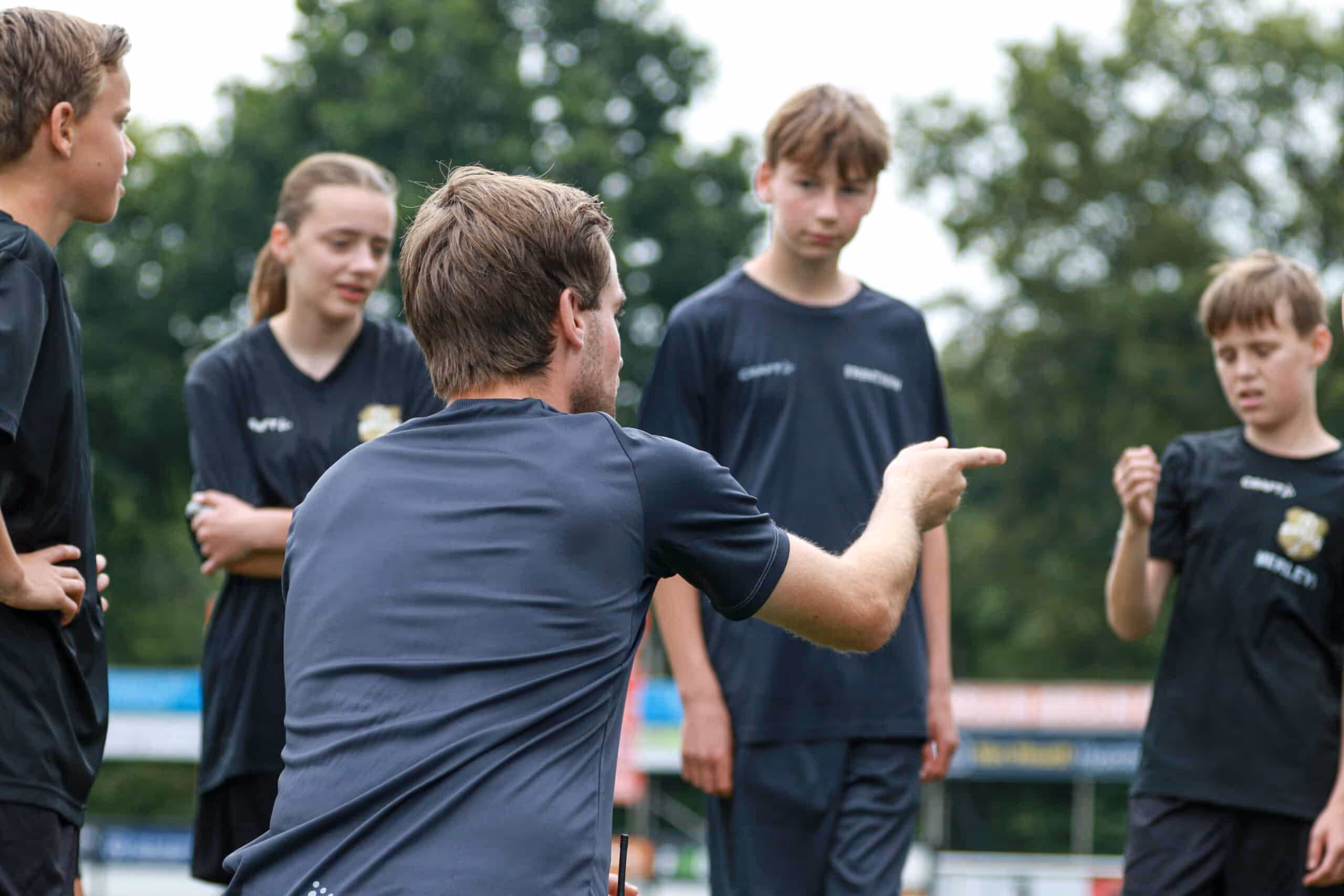 Een sportprofessional van sportmarketingbureau FrontRow die de tactiek op het voetbalveld bespreekt met de kinderen
