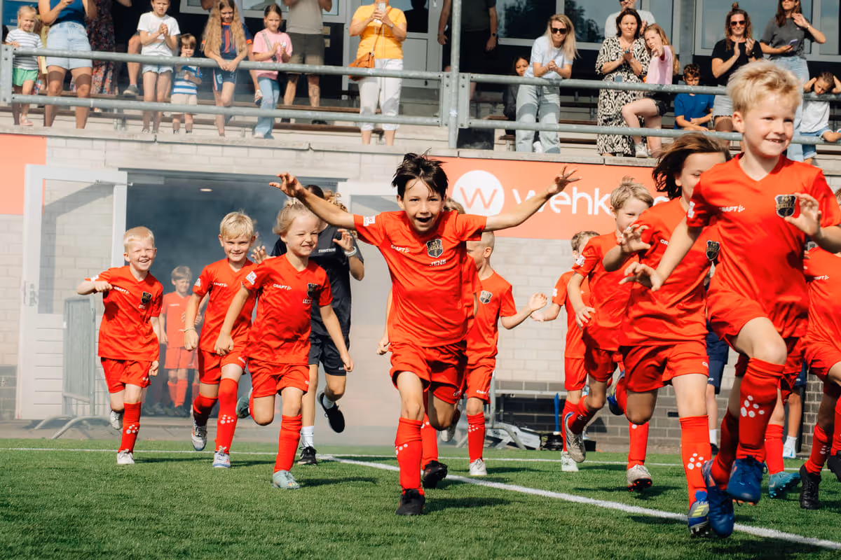 Een groep vrolijke kinderen met mascotte Binkie tijdens een B2C sportevenement op het voetbalveld
