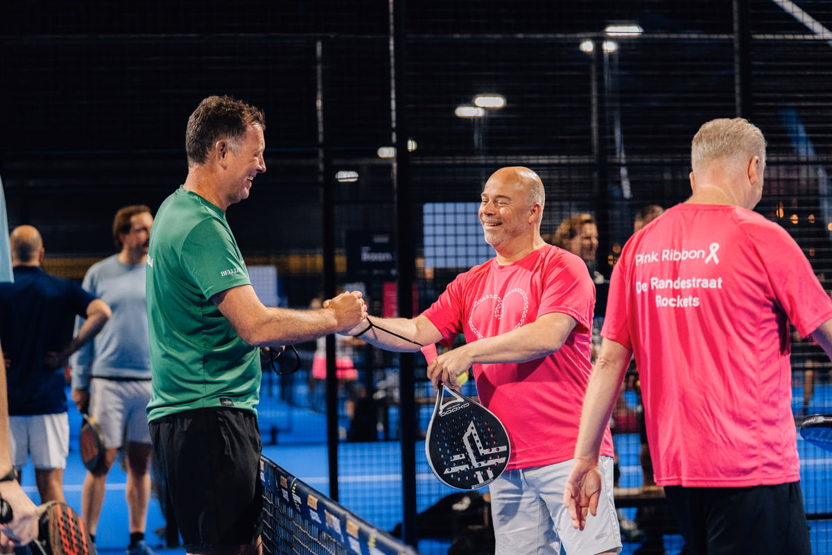  Padelspelers geven elkaar een sportieve handdruk tijdens het Pink Ribbon toernooi.