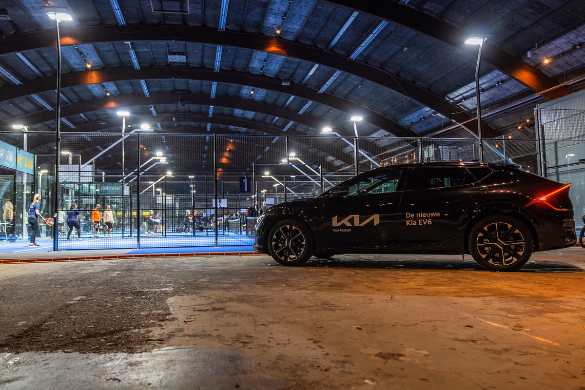 De nieuwe Kia EV6 van partner Van Mossel Kia staat geparkeerd naast een verlichte indoor padelbaan tijdens het business padel event Kerst met Ballen, georganiseerd door sportmarketingbureau FrontRow.