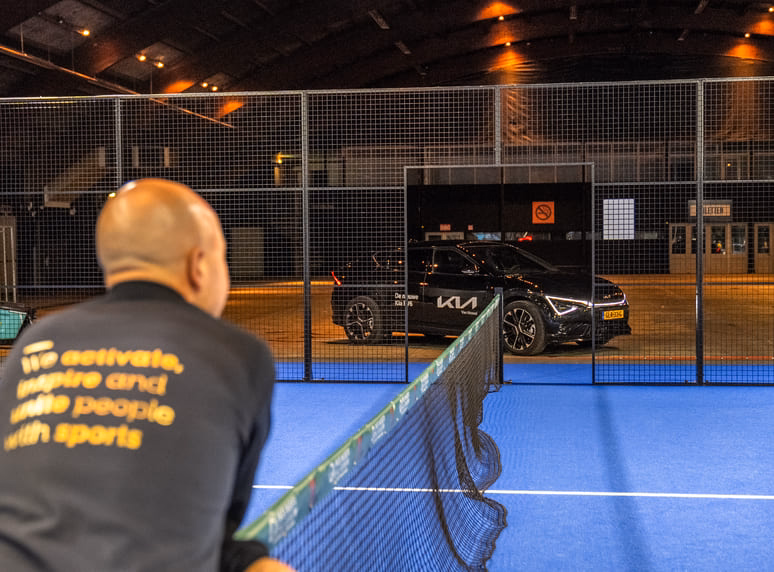 Eigenaar van sportmarketingbureau FrontRow kijkt uit over de padelbaan tijdens het business padel event Kerst met Ballen, met partner Van Mossel Kia zichtbaar op de achtergrond met een zwarte auto naast de baan.